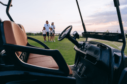 Golf cart’s steering and seat in focus, family standing behind